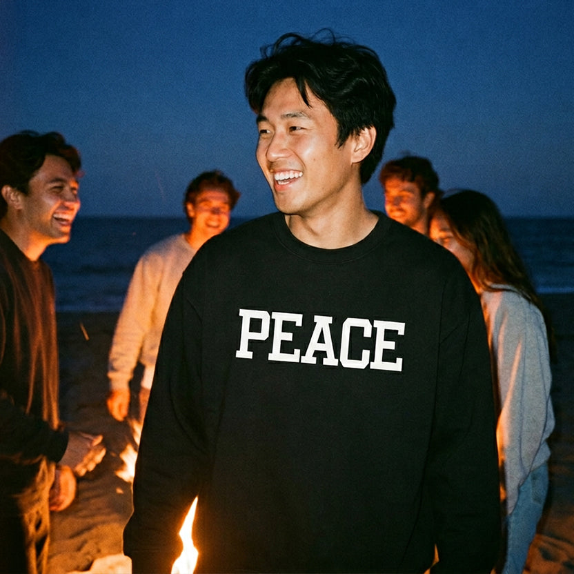 Person wearing a black 'PEACE' shirt at a bonfire with friends on a beach at night.