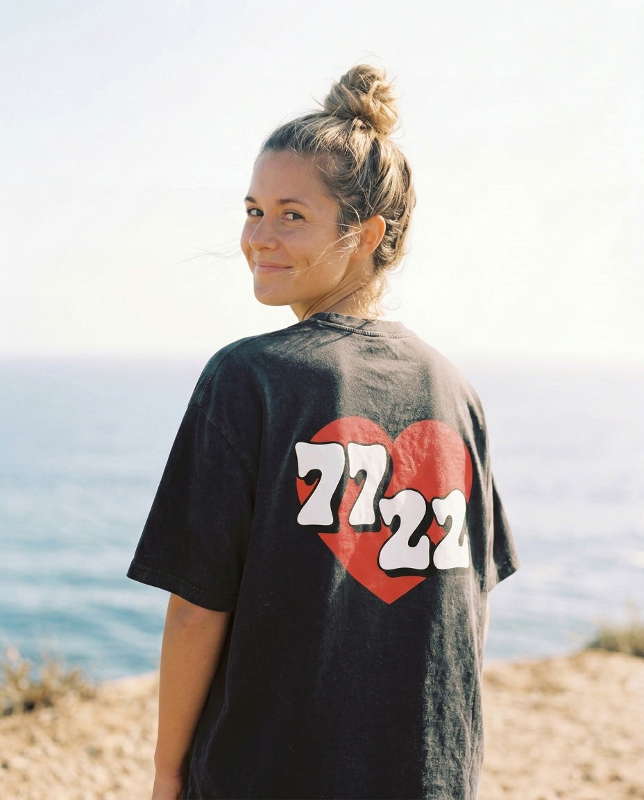 Person wearing a black t-shirt with a red heart and numbers by the beach