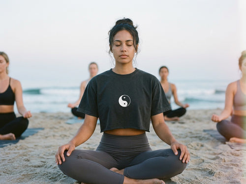 Woman practicing yoga on a beach with others in the background wearing a Yin Yang design crop top