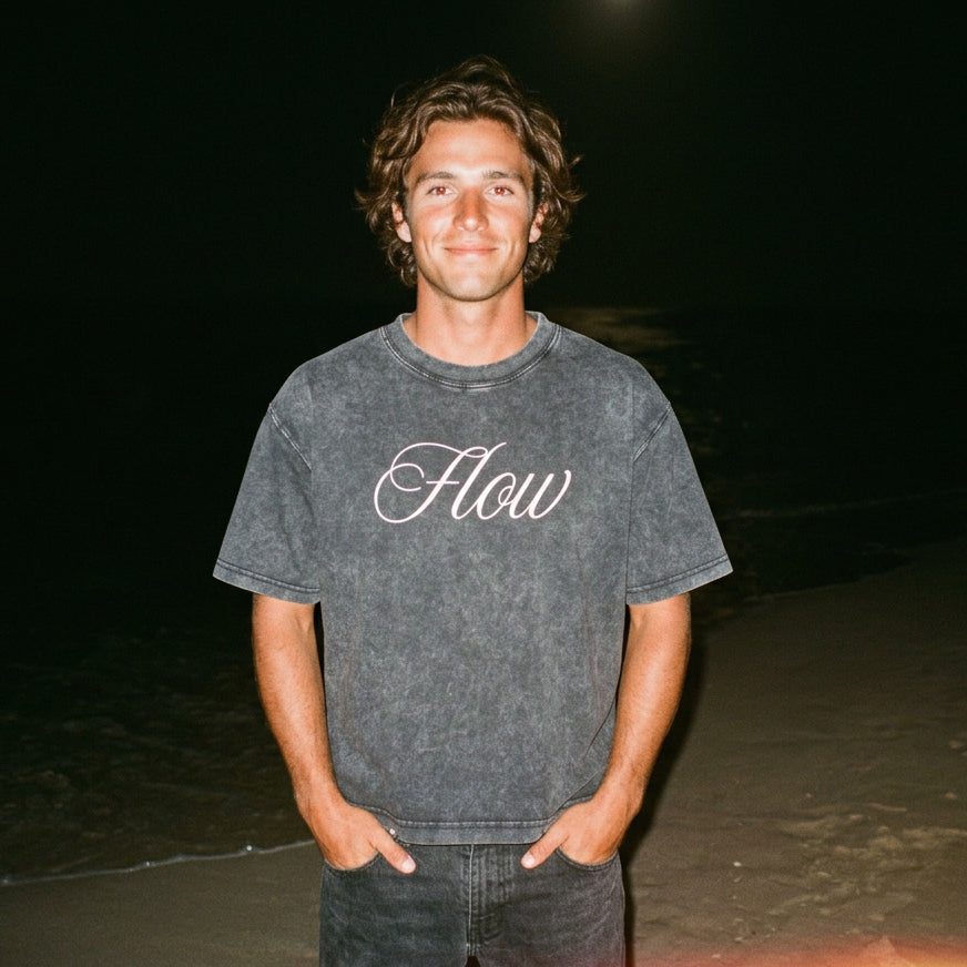 Person wearing a black mineral washed t-shirt with 'Flow' printed on it against a dark background