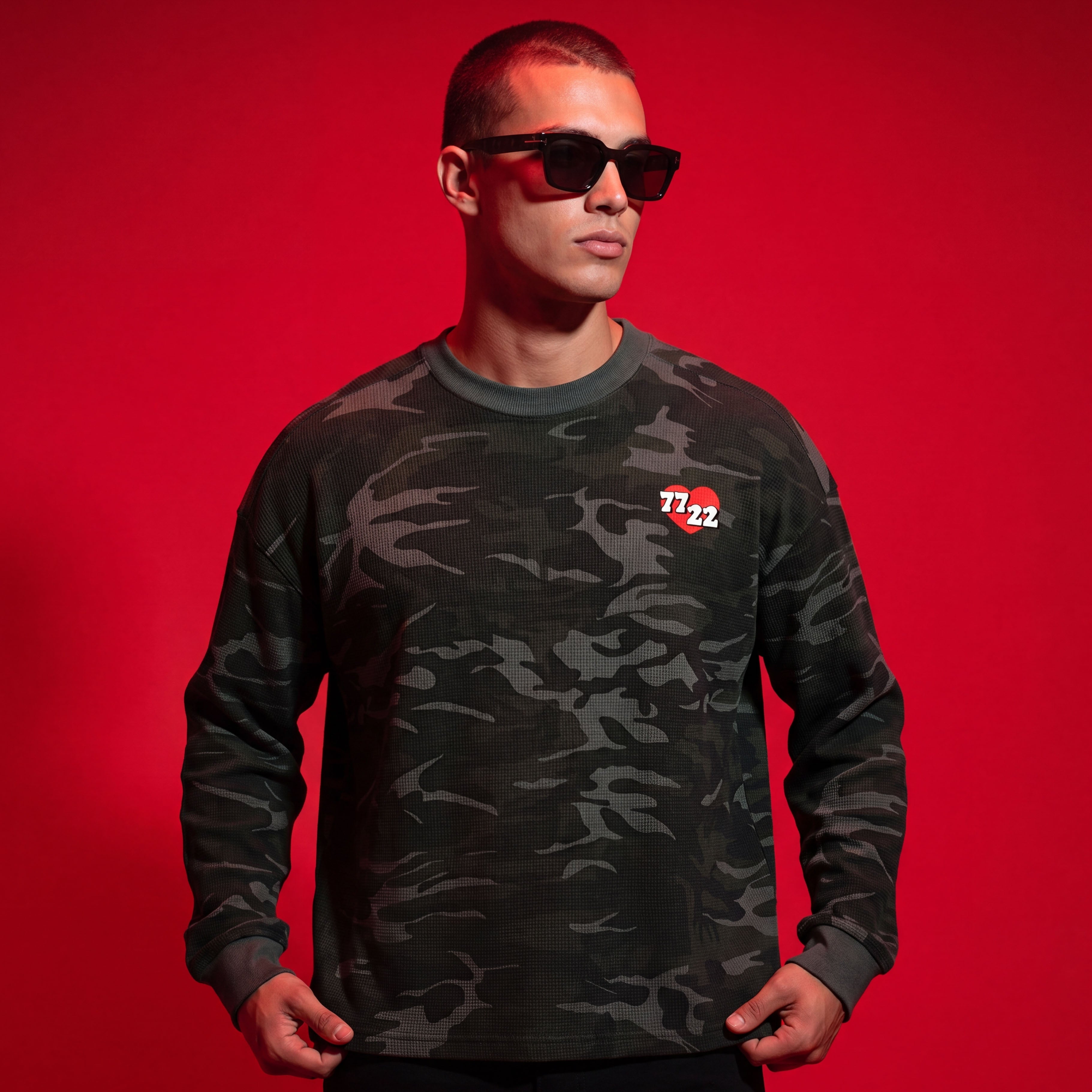 Person wearing a camouflage long-sleeve shirt with a logo on a red background