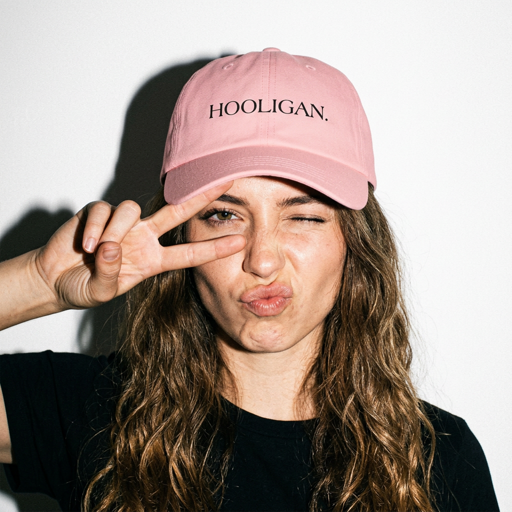 Person wearing a pink cap with 'HOOLIGAN' text, making a peace sign.