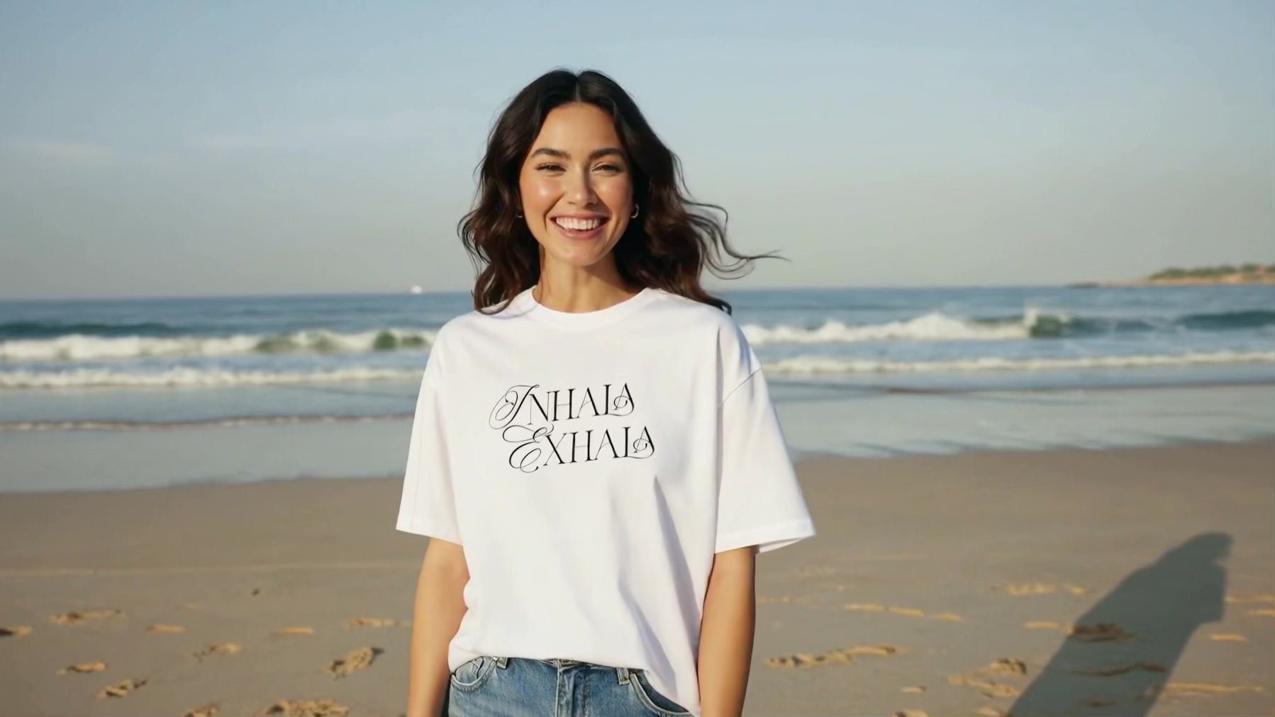 Woman walks on beach laughing wearing INHALA EXHALA graphic tee.