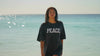 Girl wearing PEACE t-shirt walks on beach and runs hand through hair.